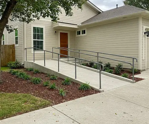 Concrete wheelchair ramp with metal handrails and mulched planting beds at a home entrance