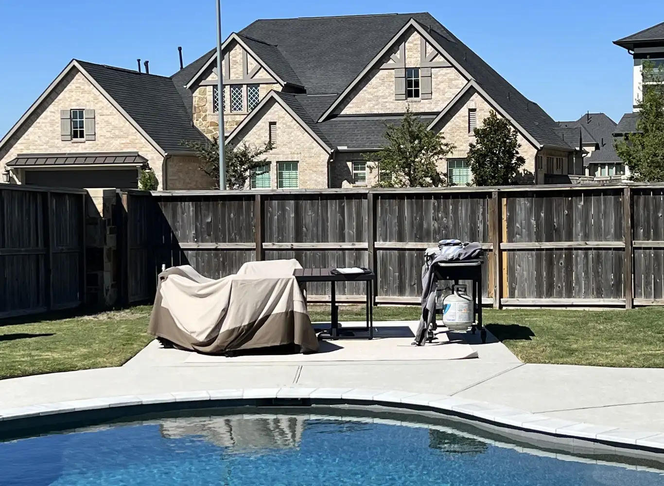 Before: plain concrete pool deck with a covered grill, patio furniture and a wood privacy fence