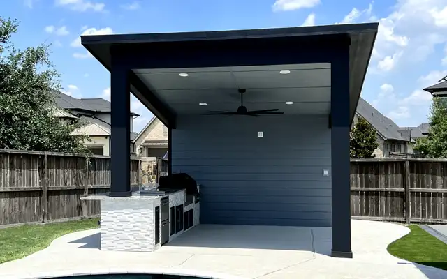 Modern dark pavilion with ceiling fan and stone-clad outdoor kitchen next to a pool