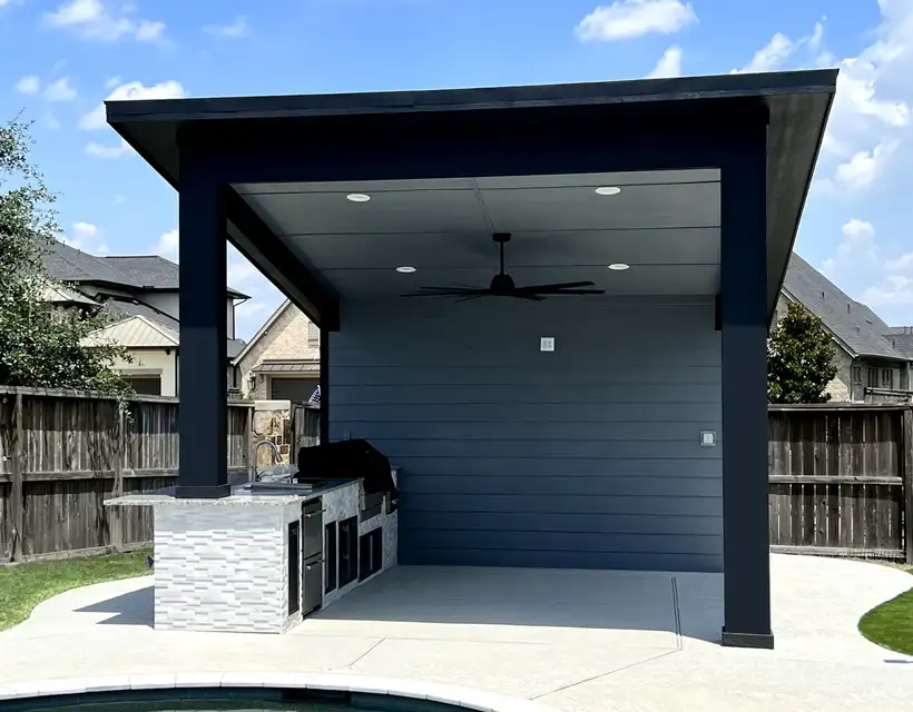 Modern shed-roof pavilion with ceiling fan and stone-clad grill island beside a pool