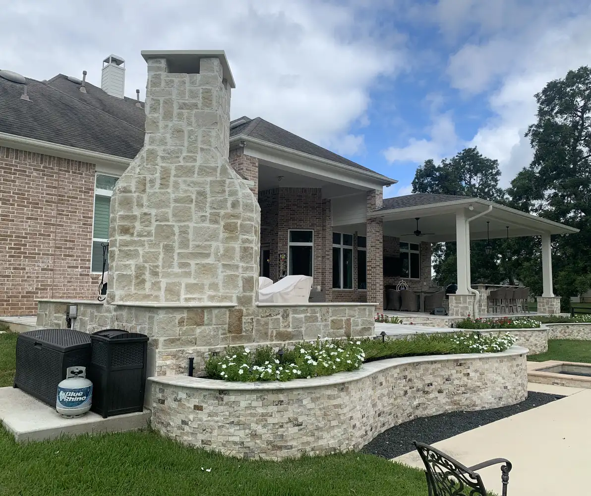 Stacked limestone outdoor fireplace beside a curved stone planter wall filled with flowers