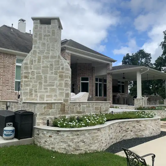 Stacked stone outdoor fireplace and curved stone planter wall at a Houston backyard patio