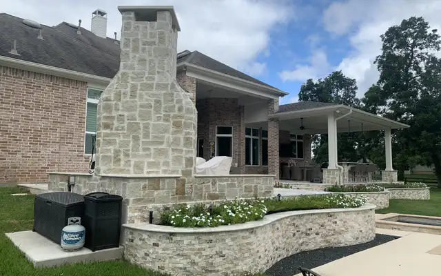 Tall stacked limestone outdoor fireplace chimney with a curved split-face stone planter wall, built by HLI
