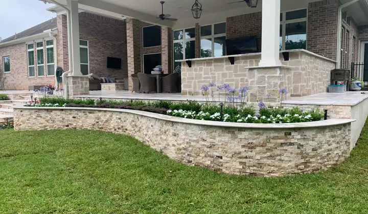 Curved stacked stone planter wall with flowers below a large covered patio on a Houston home