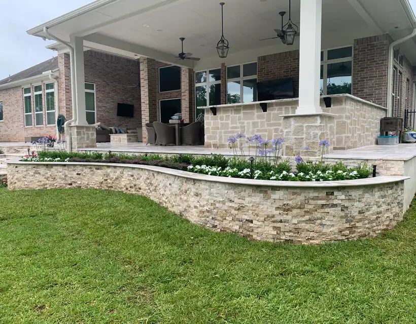 Curved split-face stone planter wall with white flowers below a large covered patio at the Adamson residence
