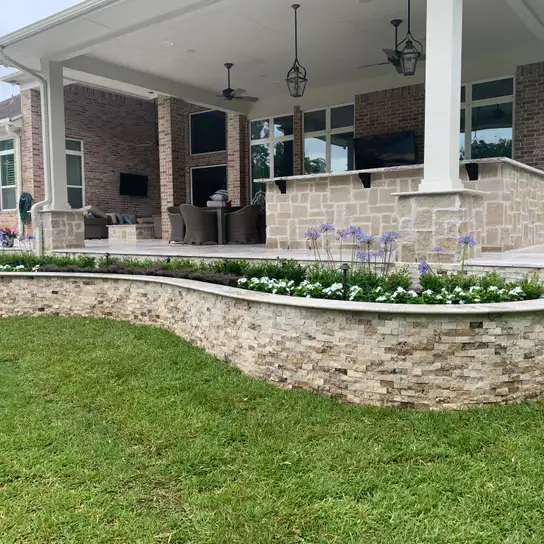 Curved stacked stone planter wall with flowers below a large covered patio on a Houston home