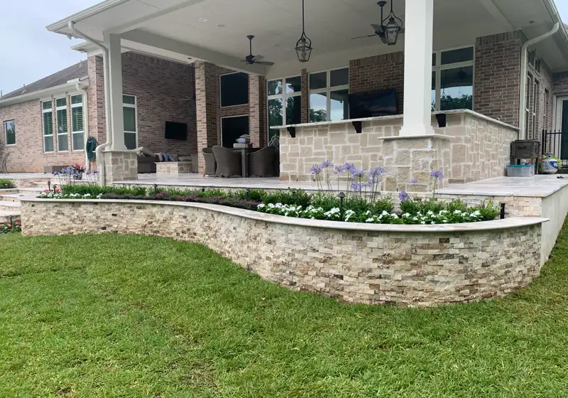 Curved stacked stone planter wall with flowers below a large covered patio on a Houston home