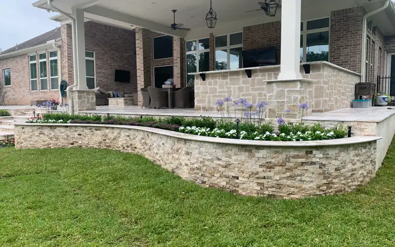 Curved stacked stone planter wall with flowers below a large covered patio on a Houston home