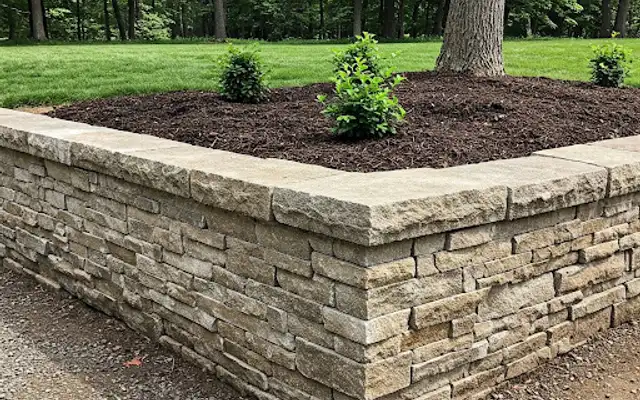 Dry-stacked natural stone raised bed border filled with mulch and young shrubs