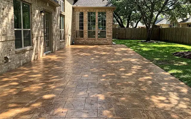 Tan stamped concrete patio in an ashlar slate pattern behind a brick home