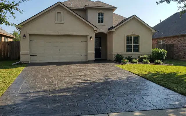 Dark gray stamped concrete driveway leading to a stucco home garage