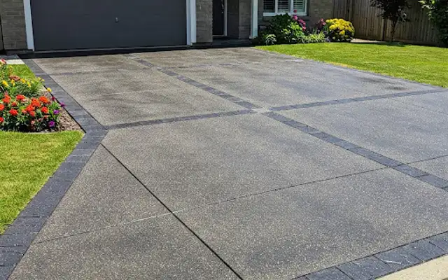 New concrete driveway with dark paver border bands leading to a two-car garage