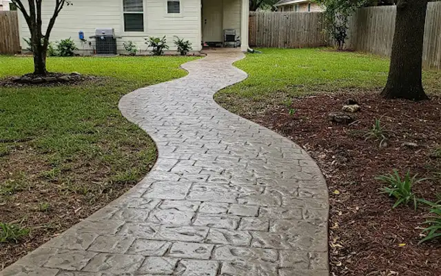Curving gray stamped concrete walkway winding through a lawn to a house