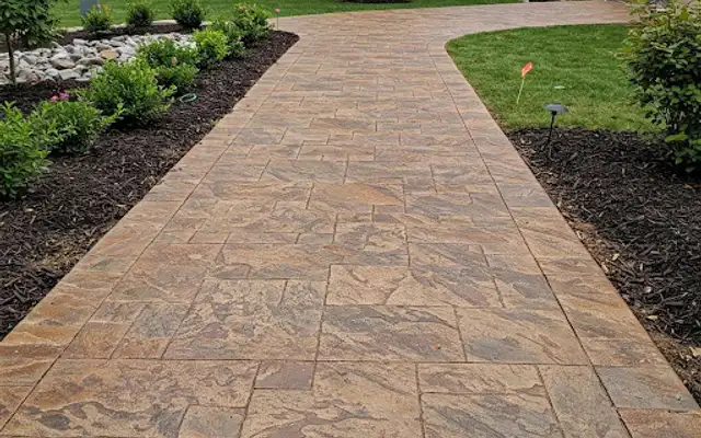Wide tan stamped concrete walkway bordered by mulched plant beds