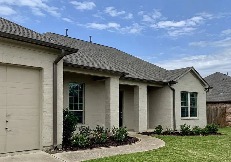 Painted brick home with gutters, downspouts and freshly mulched foundation shrub beds