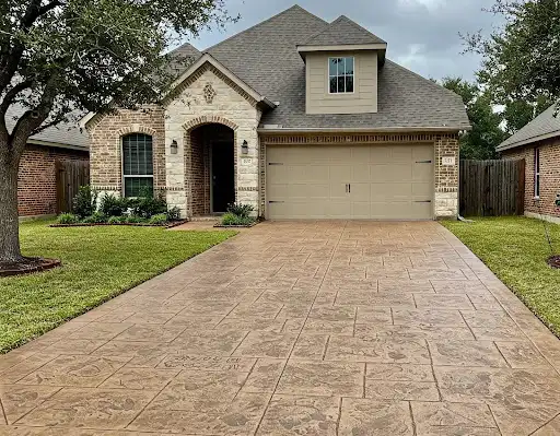 Tan stamped concrete driveway leading to a brick and stone home garage