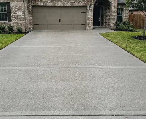 Smooth gray concrete driveway leading to a brick home with a tan garage door