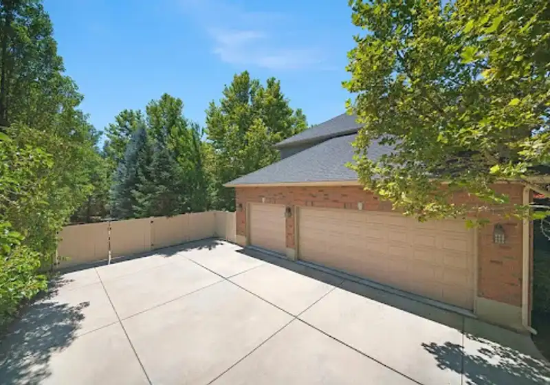 Large concrete driveway pad in front of a three-car garage surrounded by trees