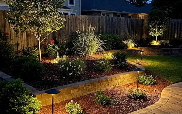 Mulched plant beds with a block retaining wall and path lights at night