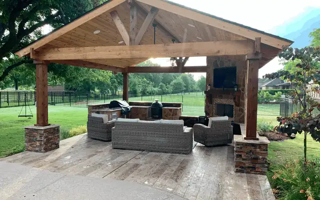 Cedar gable gazebo on stone column bases with a fireplace, TV and wicker seating