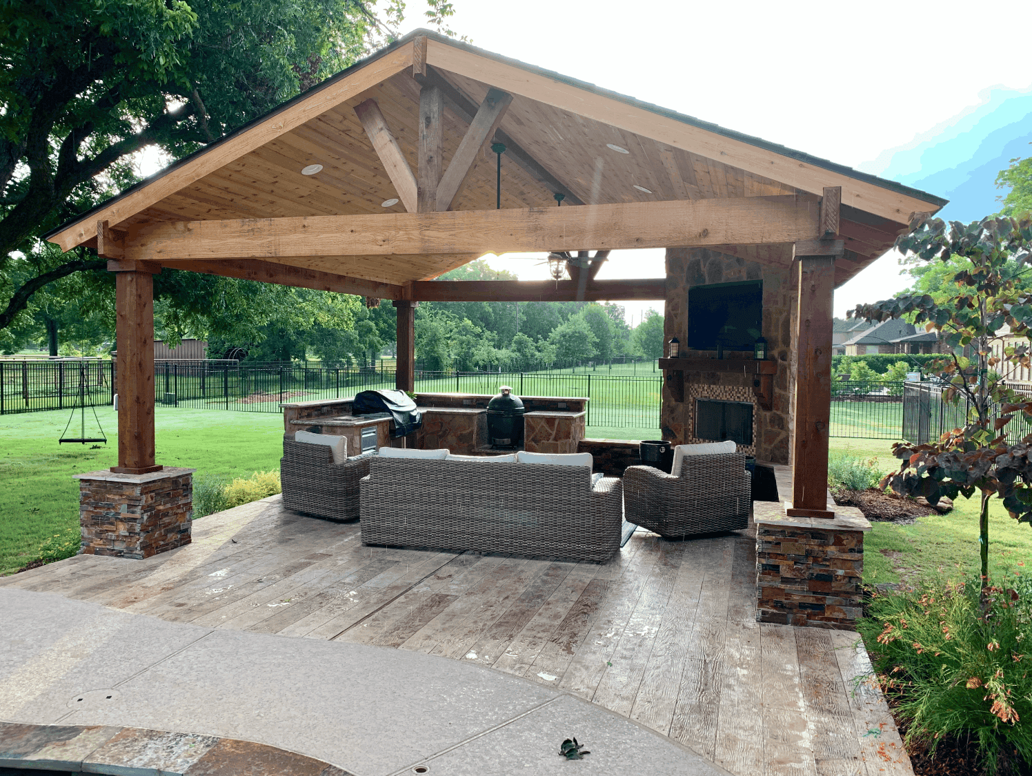 Cedar pavilion with stone fireplace, mounted TV and wicker seating on a stamped concrete patio