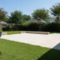 Light tan paver patio surrounded by green lawn and crape myrtles in a backyard