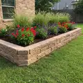 Raised stone block planter wall filled with red and purple flowers beside a green lawn