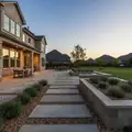 Backyard at dusk with concrete stepping-stone path, low planter wall and patio seating