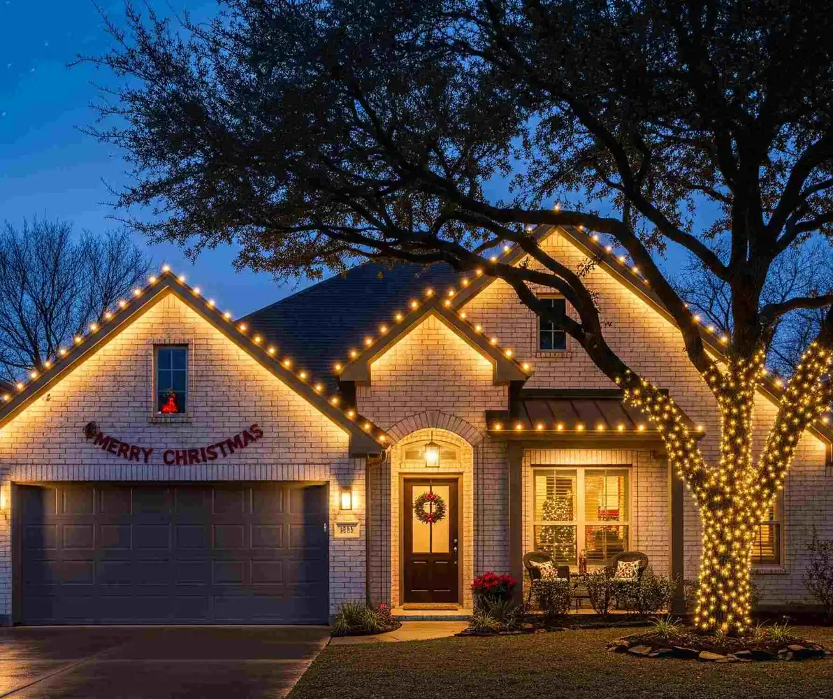 Brick home with warm white roofline Christmas lights and a light-wrapped oak tree at night