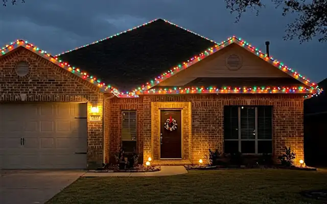 Brick ranch house with multicolor roofline Christmas lights and a wreath on the front door at dusk