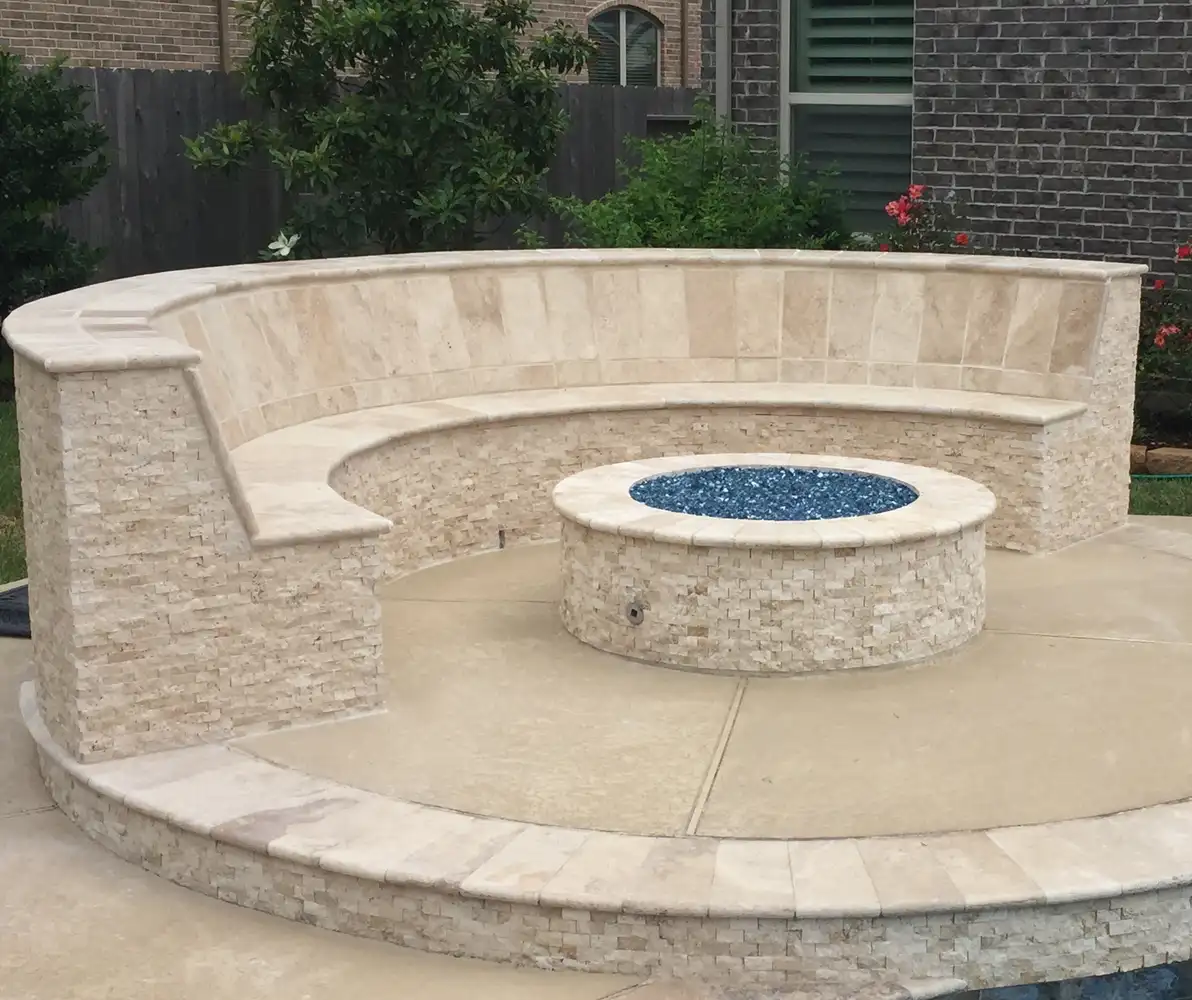 Stacked stone fire pit with blue fire glass and a curved seat wall beside a Houston pool
