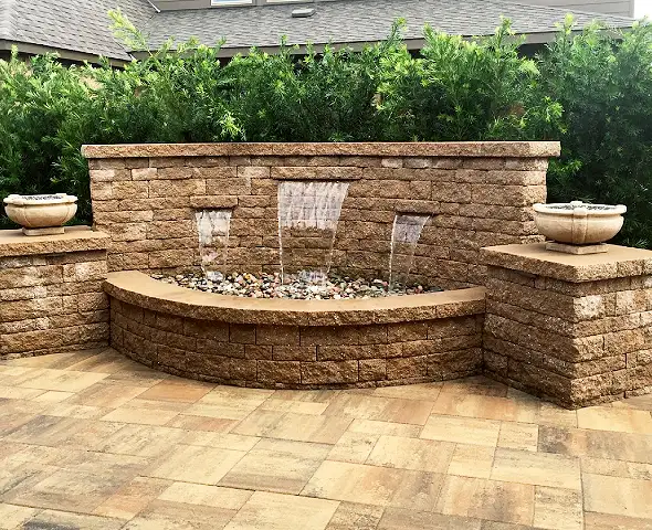 Segmental block wall fountain with three sheer spillways and stone urns on a paver patio, built by HLI