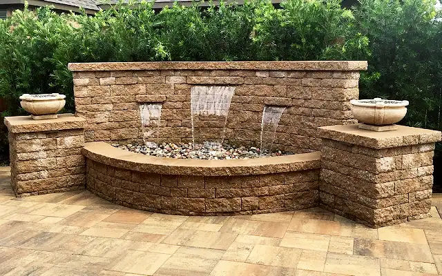 Block wall fountain with three sheer spillways into a curved basin on a paver patio, built by HLI