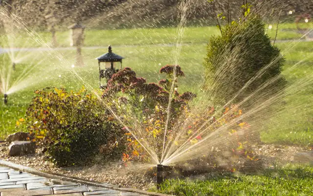 Pop-up sprinklers spraying a flower bed and lawn beside a paver path