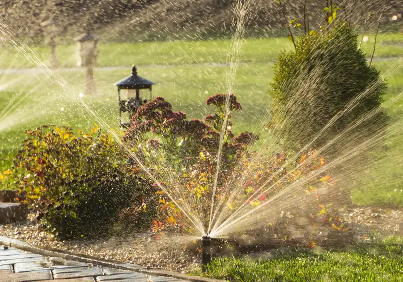 Pop-up sprinkler heads watering a flower bed and lawn beside a paver path