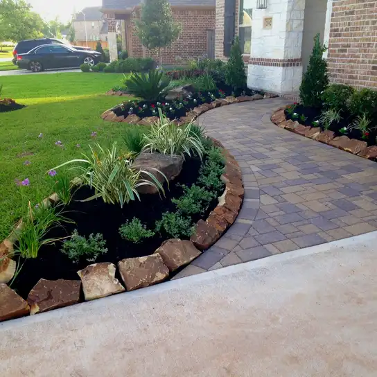 Curved paver walkway with boulder-edged planting beds at a Houston home entry