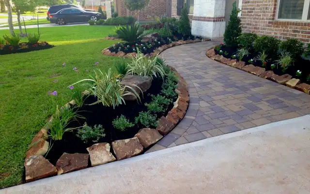 Front yard landscape design with a curved paver walkway, boulders and mulched planting beds