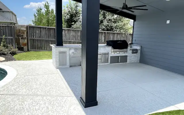 Artificial turf beside a textured pool deck and dark modern outdoor kitchen pavilion