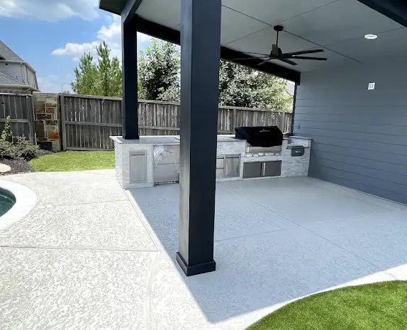Modern dark pavilion over an outdoor kitchen with a textured pool deck and artificial turf