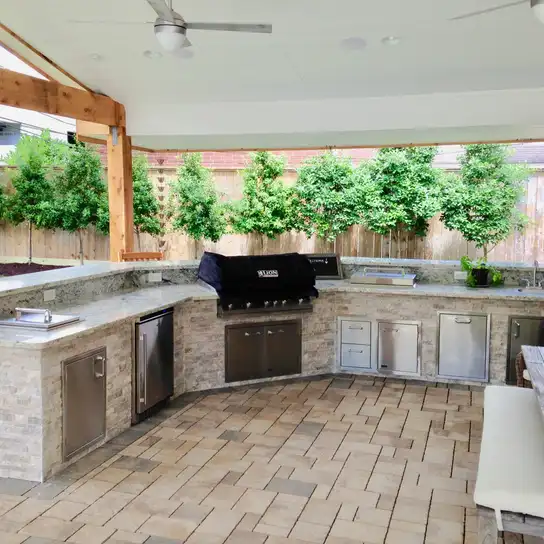 L-shaped stone outdoor kitchen with built-in grill under a cedar patio cover