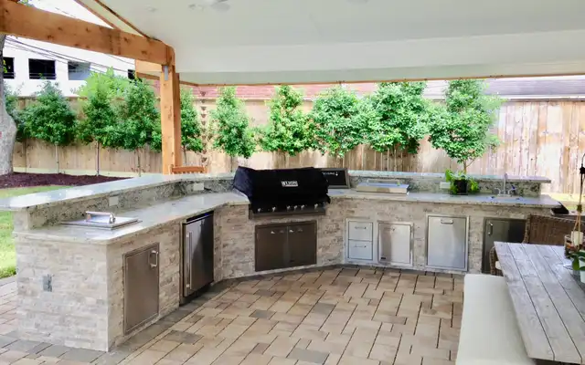 L-shaped stacked stone outdoor kitchen with built-in grill and stainless doors under a cedar cover
