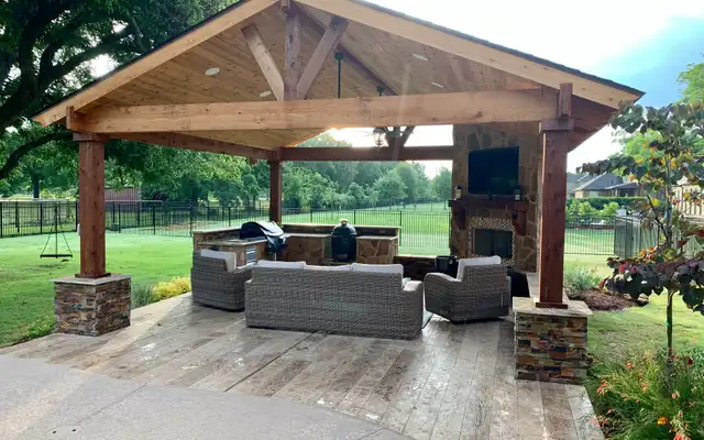Cedar gable pavilion on stone column bases with outdoor fireplace, TV and wicker seating, built by HLI