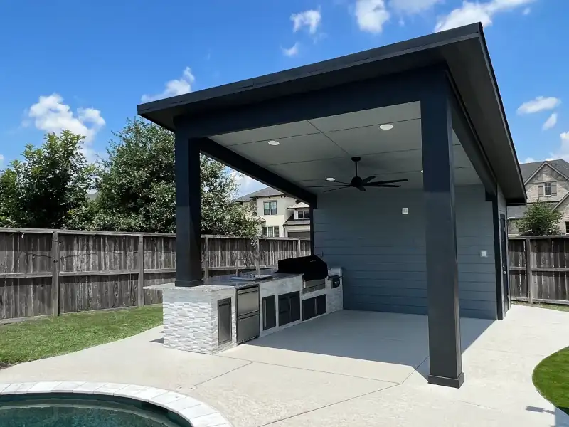 Modern dark pavilion with ceiling fan and outdoor kitchen beside a backyard pool