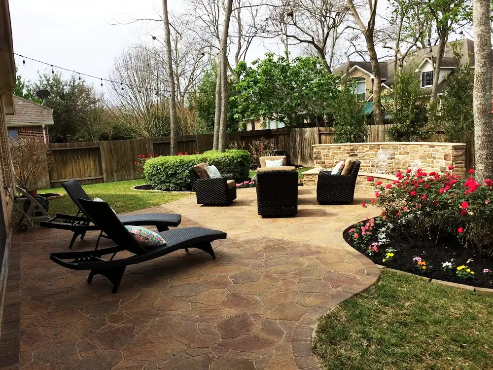 Stamped flagstone-pattern patio with lounge chairs, stone seat wall and rose beds in a Houston backyard