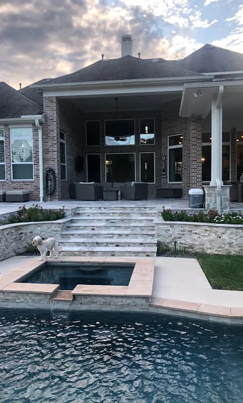 Travertine steps and stacked stone planter walls leading from a covered patio to a pool spa