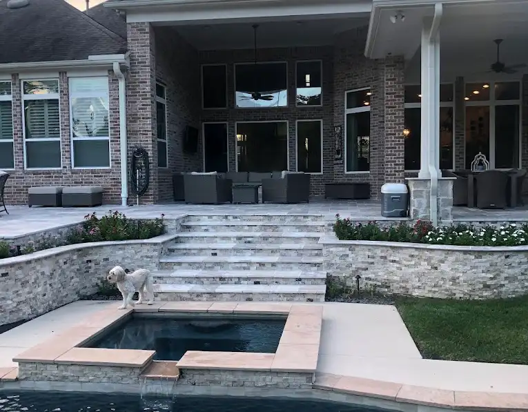 Travertine steps and stacked stone planter walls leading from a covered patio to a pool spa