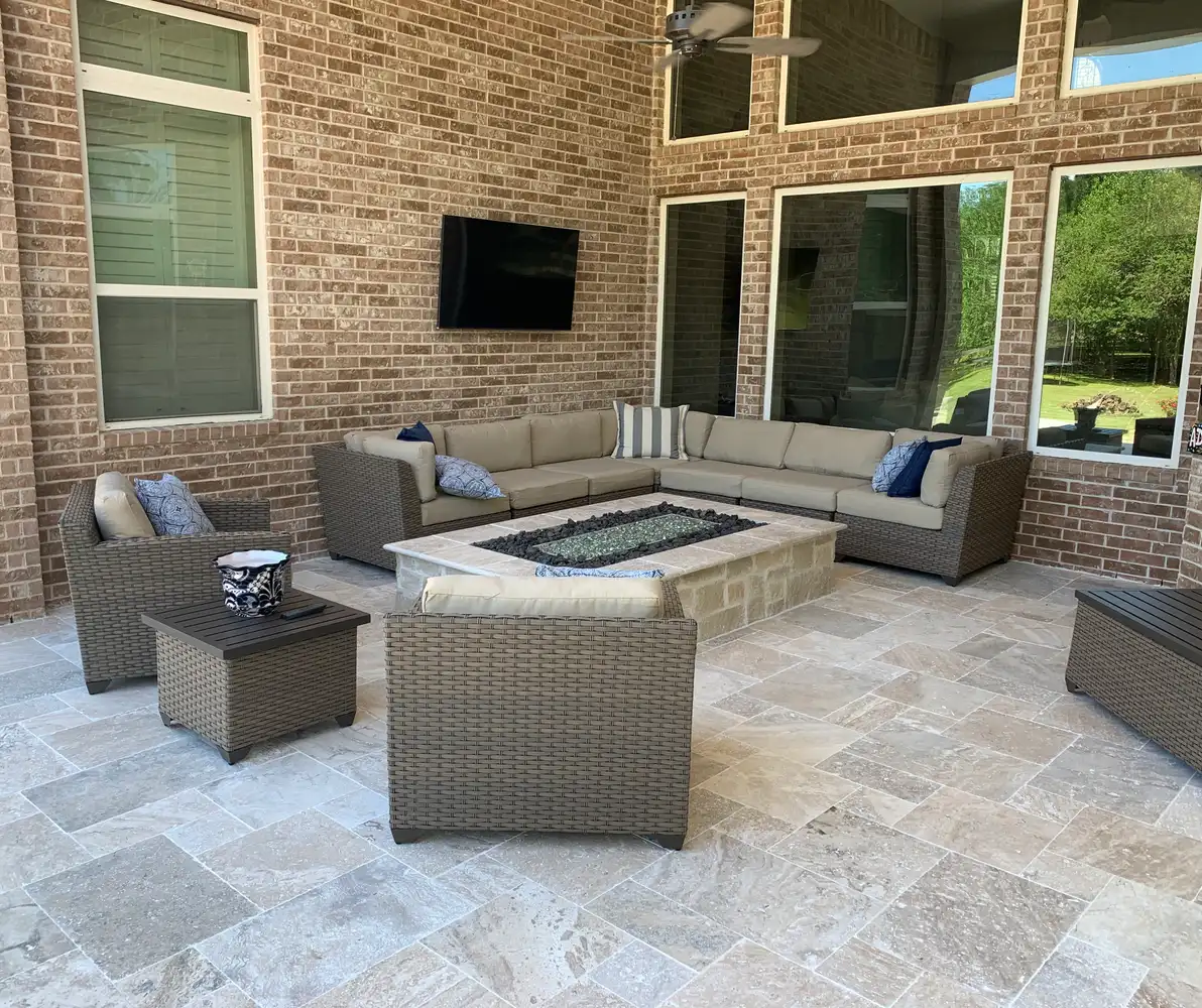 Travertine covered patio with a stone fire table, wicker sectional and wall-mounted TV