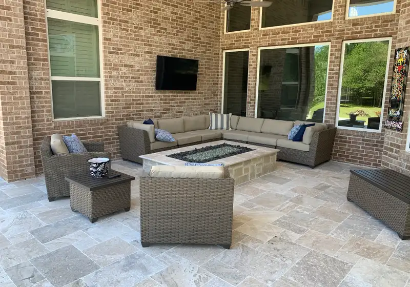 Travertine paver covered patio with stone fire table and wicker sectional seating