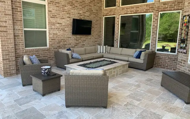 Stone fire table with a wicker sectional on a covered travertine paver patio, built by HLI