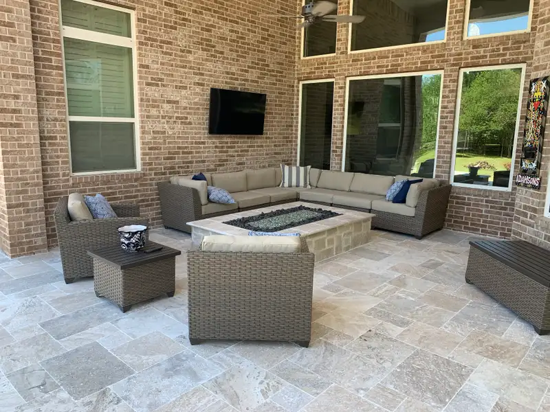 Covered travertine paver patio with stone fire table and wicker sectional seating